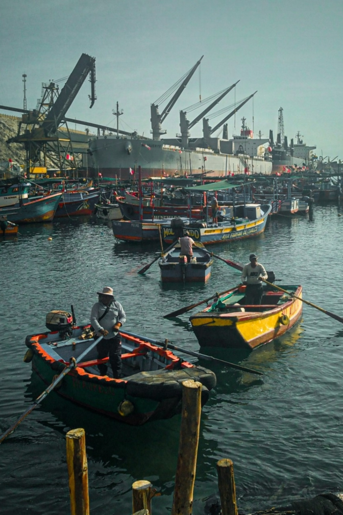 Colorful fishing boats in a bustling harbor with a large ship and cranes.